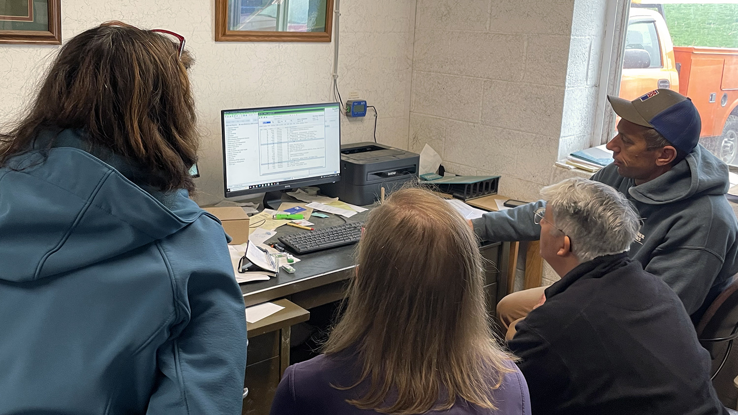 DRMS staff gather around a dairy farmer's computer to demonstrate their software.